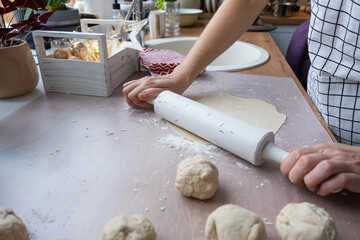 Hands knead thick dough, roll out with a rolling pin on the kitchen table, decorated with festive decorations for Christmas and New year. Baking at home, aroma and comfort. 
