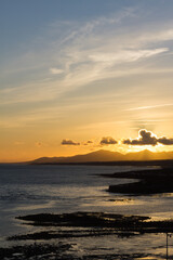 Backlight of mountains over the sea at sunrise. The golden sun sets behind the silhouettes of the mountains. Golden clouds over the ocean. Lanzarote, Canary Islands, Spain.