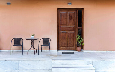 A contemporary house entrance, with a natural wood door, a small table and two chairs on the...