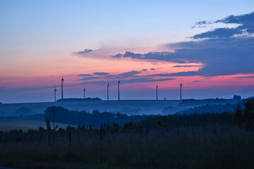 foggy sunrise over the fields with wind turbines in the landscape