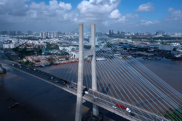 Obraz premium Aerial view of Phu My Bridge over Saigon river with road and river transportation on a sunny day. Cables catch light. High angle featuring roadway and heavy vehicles and Ho Chi Minh City skyline 