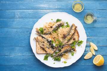 Marinated  sardines or Sarde in saor, a typical dish from the Venice, Italy  with white onions marinated with wine vinegar, raisins and pine nuts, served with bread. Blue marine wooden table. Copy spa