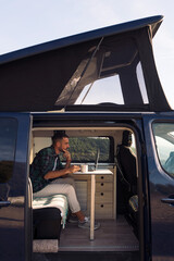 young man sitting in his camper van working on his laptop, concept of freedom and digital nomad...