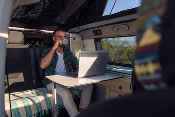 young man working on his laptop from his camper van, concept of freedom and digital nomad lifestyle