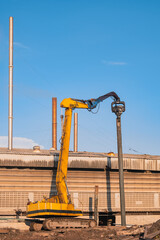 Yellow Pile drilling crawler crane working to install foundation pole near the old factory building in industrial construction site