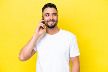 Young Arab handsome man isolated on yellow background keeping a conversation with the mobile phone...
