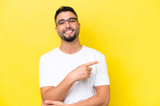 Young Arab handsome man isolated on yellow background With glasses and pointing side