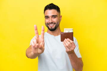 Young Arab man holding a wallet isolated on yellow background smiling and showing victory sign