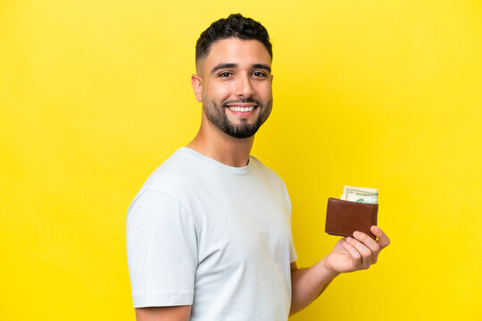 Young Arab Man Holding A Wallet Isolated On Yellow Background Smiling A Lot