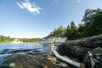 View with white cruise boat moored in rocky shore surrounded by lush pine trees under blue sky