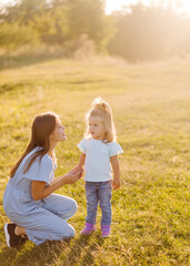 Young mother and daughter, hugging and playing in a golden field of sunshine