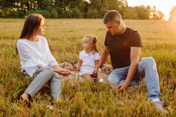 Happy family in a field in autumn. Mother, father and baby play in nature in the rays of sunset.