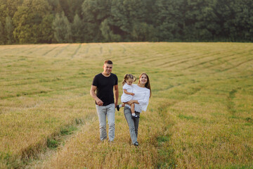 Naklejka na ściany i meble Happy family in a field in autumn. Mother, father and baby play in nature in the rays of sunset