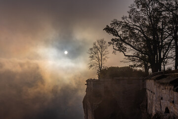 Fels der Festung Königstein am Morgen im Nebel im Herbst mit Sonne hinter den Wolken