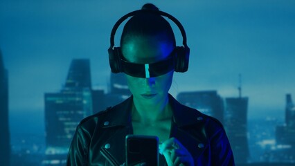 Portrait of cyberpunk girl with a smartphone in a glasses and headphones. Beautiful young woman on...