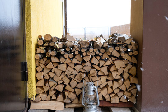 The firewood on the snowy porch of the house is harvested for the winter. Heating of housing with a stove fireplace, saving electricity and gas in a crisis, environmental friendliness.