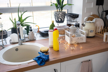 Cleaning the kitchen before the Christmas and New Year holidays. Detergent, dry powder, sponge, gloves are on the sink. Festive decor in the white kitchen, cozy interior of the home