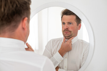 young man with a double chin examing his reflection in mirror - obrazy, fototapety, plakaty