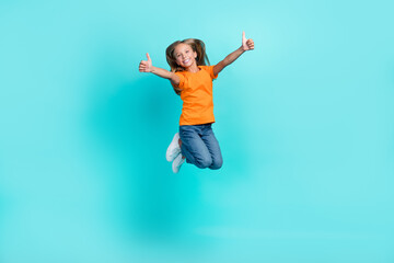 Full length photo of cute funny active schoolgirl wear orange t-shirt denim jeans showing thumbs up like enjoy isolated on cyan color background