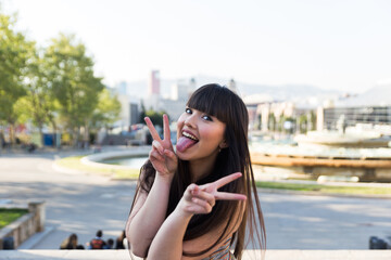 Fototapeta premium Asian european young woman with long brunette hair doing funny symbols to the camera and smiling