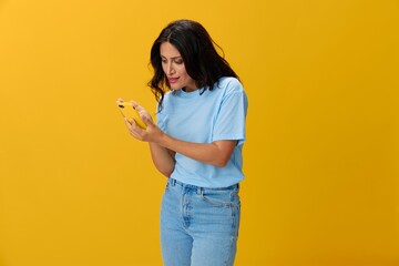 Woman blogger with a phone in her hands in a blue t-shirt and jeans on a yellow background smile signs gestures symbols, online communication and video call, copy space, free background