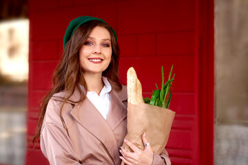 happy young smiling woman holding grocery shopping paper bag with long white bread baguette