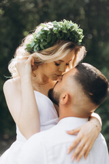 Fototapeta premium A happy young couple in love walk in a garden. A man in a white shirt and a girl in a white light dress are walking in a park