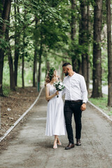 A happy young couple in love walk in a garden. A man in a white shirt and a girl in a white light dress are walking in a park