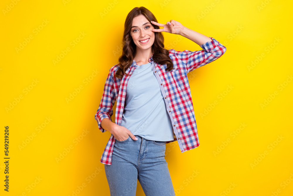 Sticker Photo of hipster pretty lady wear plaid shirt cover face v-sign photography put hand pocket denim jeans isolated on yellow color background