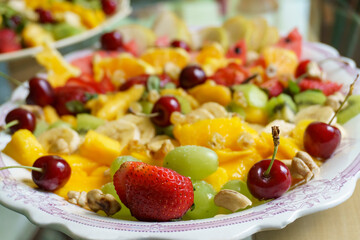 Focus on the front of tray with cut fruits, strawberries, pears, grapes, oranges, watermelon, bananas, kiwis and dried fruits.