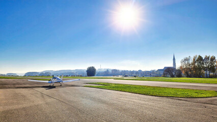 Ultraleichtflugzeug steht am Rollfeld auf einem Flugplatz an einem sonnigen Tag, Kleinstadt mit...