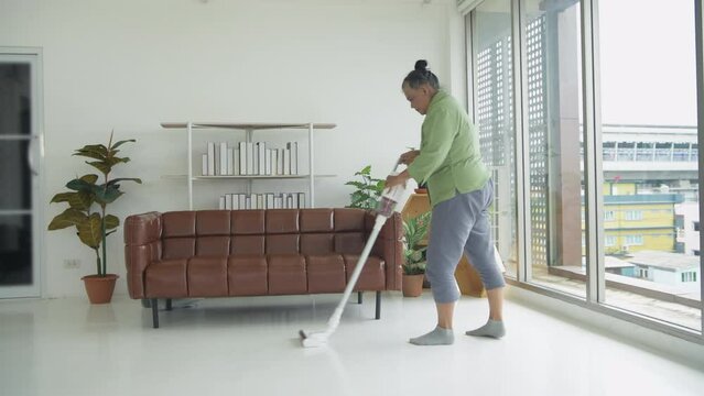 Holiday concept of 4k Resolution. An Asian old woman vacuuming inside the living room.