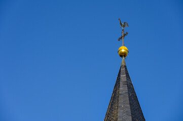 Kirchturmspitze mit Wetterhahn, Kreuz und Turmkugel vor blauem Himmel