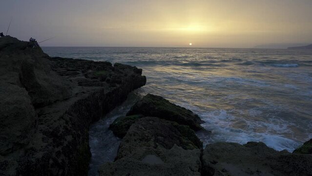 Tide waves crashing beach rocks in Tamraght  village with sunset horizon sky