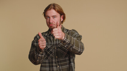 Great job, nice. Cheerful positive happy bearded man in shirt showing thumbs up and nodding in approval, successful good work. Young stylish one guy on beige studio background. People sincere emotions