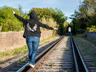 Joven mujer caminando por las vías del tren jugando a hacer equilibrio en ellas	