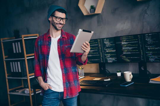 Photo of confident smiling freelancer wear hat glasses choosing stuff eshop modern gagdet indoors workplace workstation loft