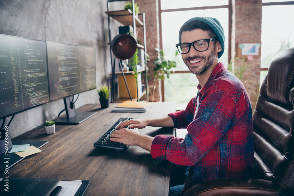 Poster photo of cheerful positive coder dressed hat glasses smiling writing system code indoors workplace w