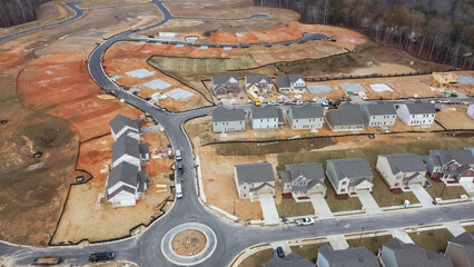 Obraz na płótnie Canvas Aerial view two story homes under construction with slope foundation, envelope houses, traffic circle, working machine and portable restroom outside Atlanta, GA, US