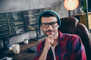 Photo of intelligent clever coder dressed hat glasses smiling arm hand chin creating program indoors workplace workstation loft