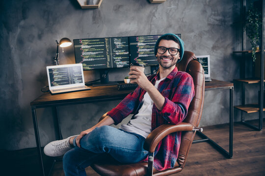 Photo of smiling positive freelancer wear hat glasses drinking beverage having rest indoors workplace workstation loft
