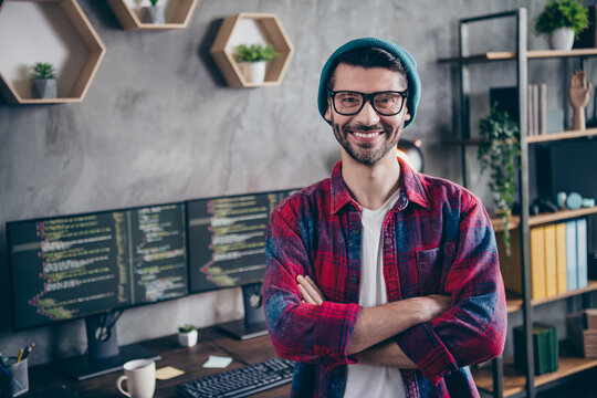 Photo of confident happy freelancer wear hat glasses arms folded smiling indoors workplace workstation loft