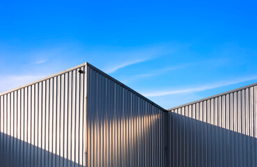 Corrugated Steel Wall of industrial Warehouse Building against blue sky background with sunlight...