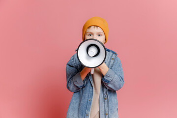 cute 7-8-year-old schoolboy in jeans and a hat, holding in his hand and speaking into an electronic...