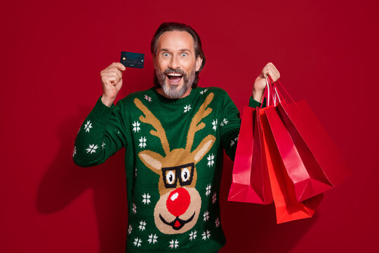Photo of excited funky man wear x-mas green sweater rising bargains credit card isolated red color background
