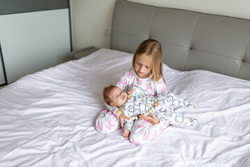 Obraz na płótnie Canvas Little sister and her baby brother. Toddler kid playing with new sibling. Girl and baby 2-3 months old relax in a home bedroom. Family with two children at home. Love, trust and tenderness concept