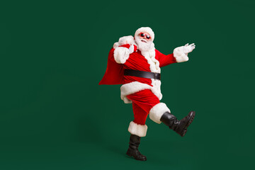 Full body profile side photo of santa claus with big belly beard carry x-mas present gift sack go wear headwear cap sunglass isolated over bright shine color background