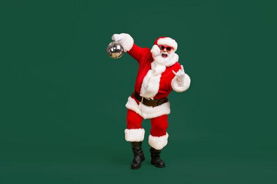 Full body photo crazy santa claus with grey beard hold disco ball show horns symbol dance x-mas christmas party wear sunglass headwear cap isolated bright shine color background