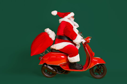 Full length profile side photo of santa claus with beard ride drive motorbike fast deliver x-mas christmas sack bag presents wear red sunglass cap isolated bright shine color background