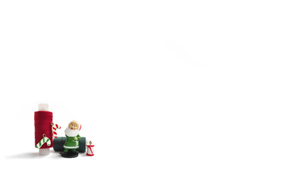 A red spool of sewing thread decorated with Christmas toys, green threads and a Santa Claus gnome on a white background.